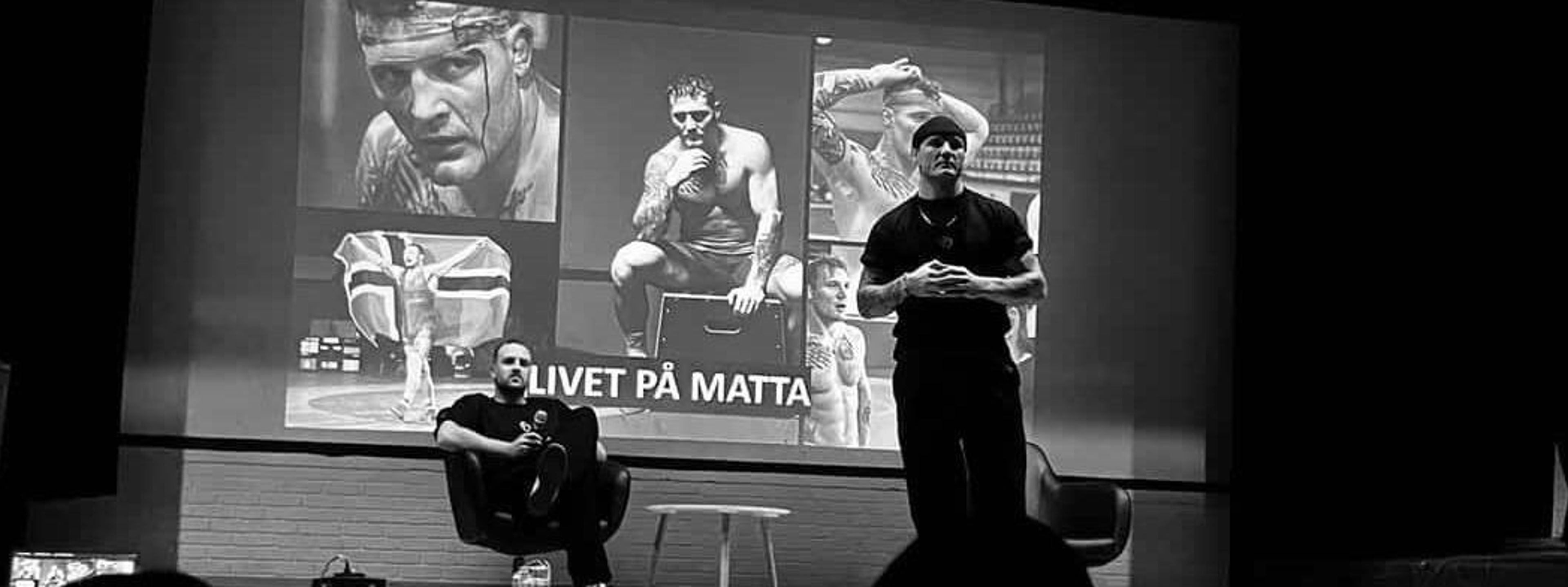 2 menn står på ei scene og held foredrag.