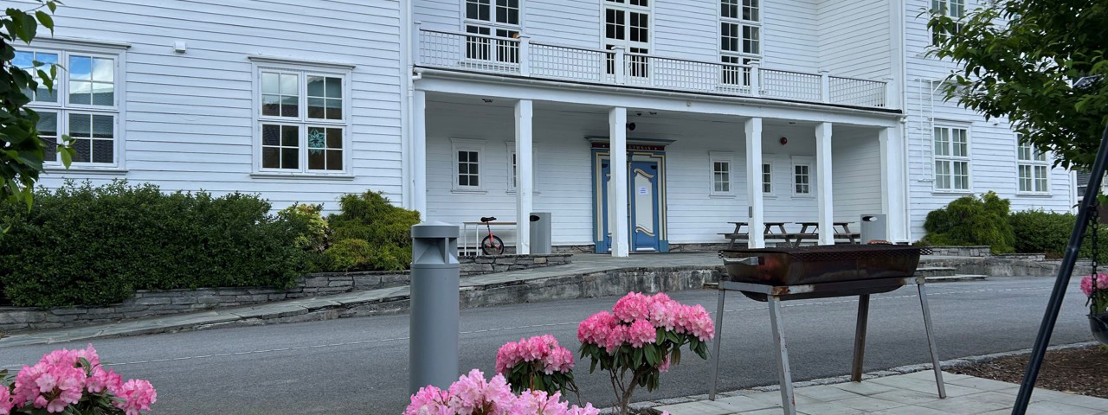 Kvitt trebygg med rosa blomar i framgrunnen.