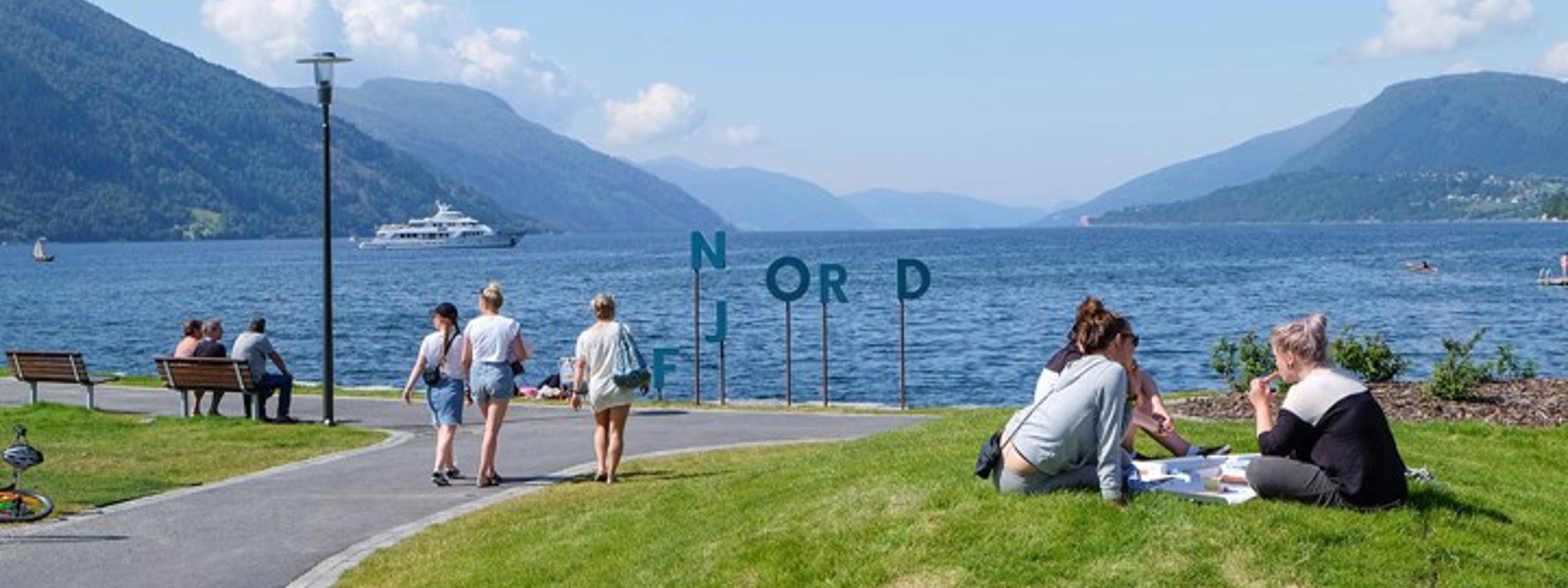 Personar som sit i graset med utsikt mot fjorden