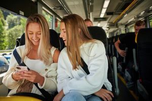 2 jenter sit i buss og ser på ein mobiltelefon