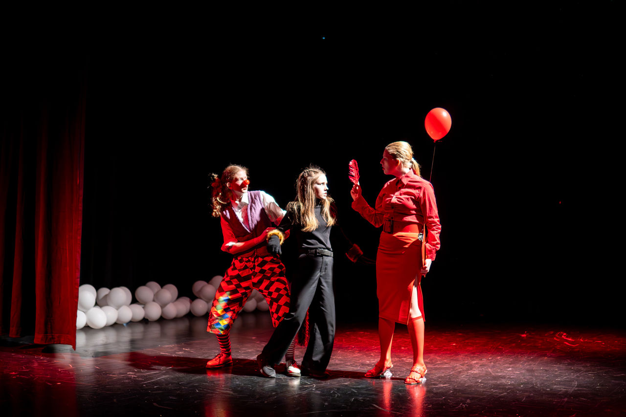 Ein klovn, ein katt og ei dame på scena med ein ballong