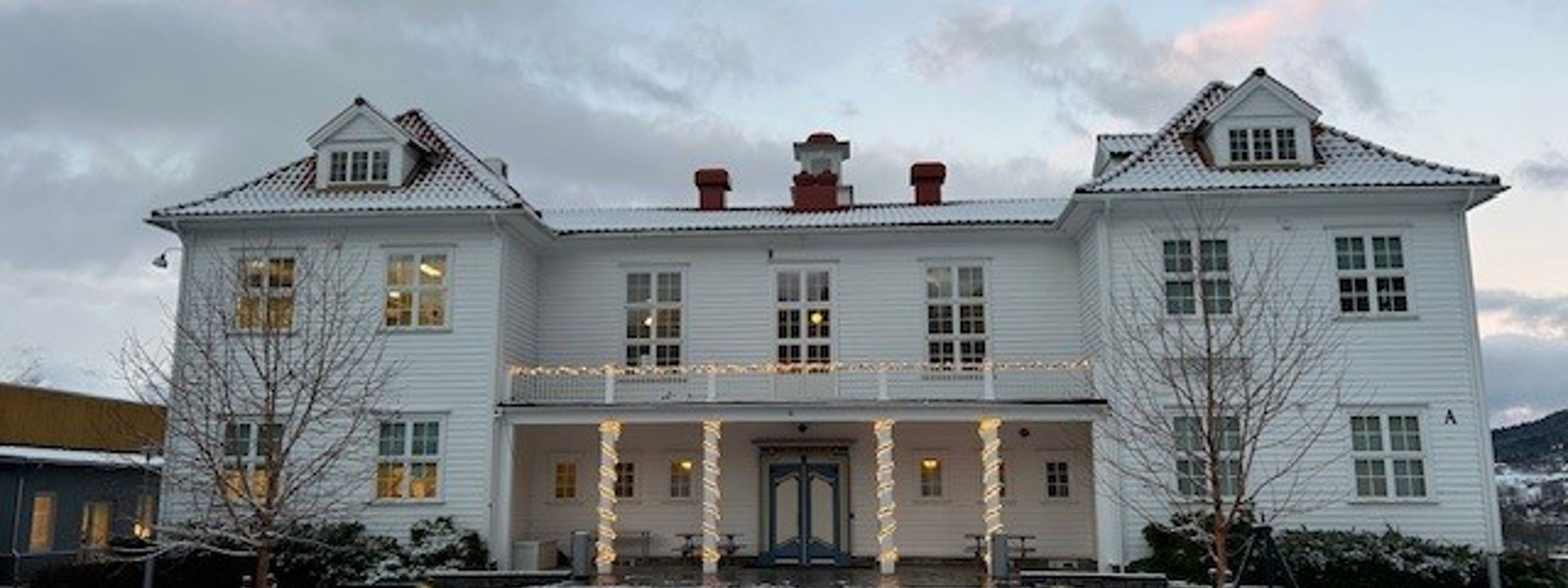 Gamlebygget på Firda vgs ( kvit trebygning) med snø i framgrunnen