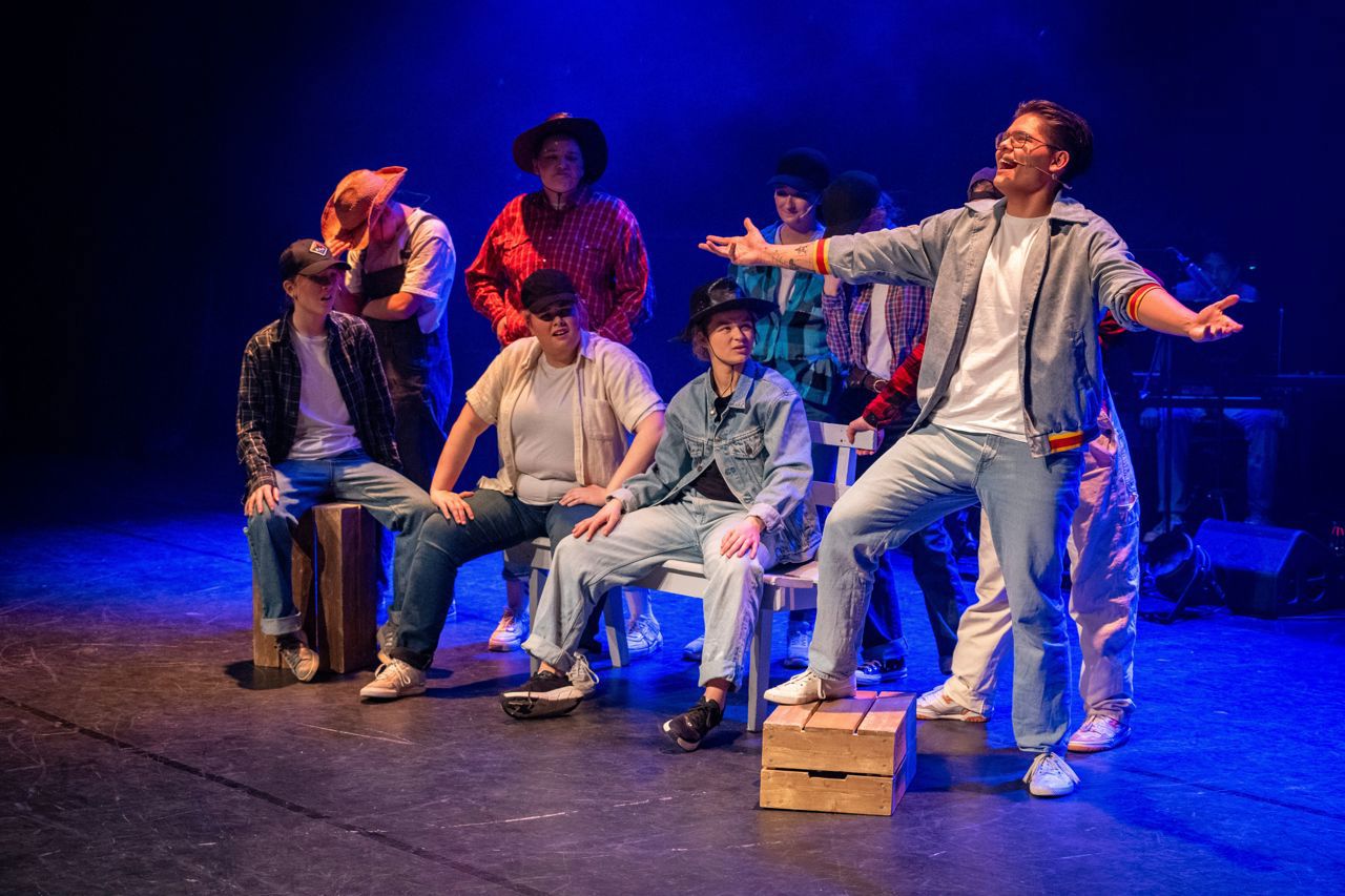 Ein elev syng på scena under musikalen Footloose. Ein gjen gutar sit i bakgrunnen.